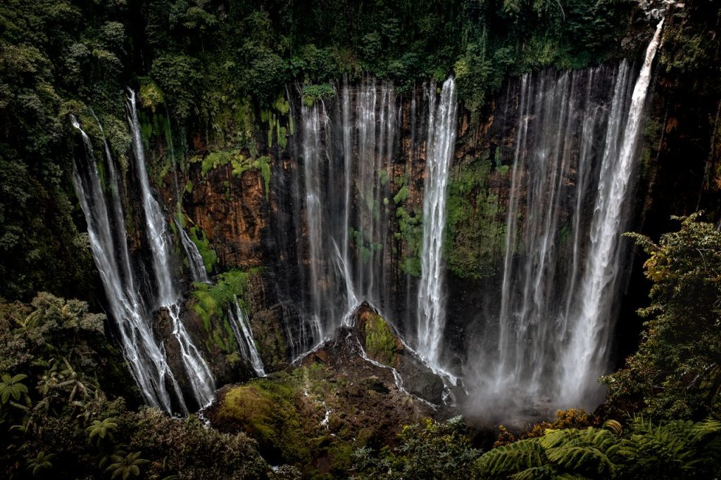 Stunning view of Tumpak Sewu Waterfall cascading in a lush jungle setting in East Java, Indonesia.